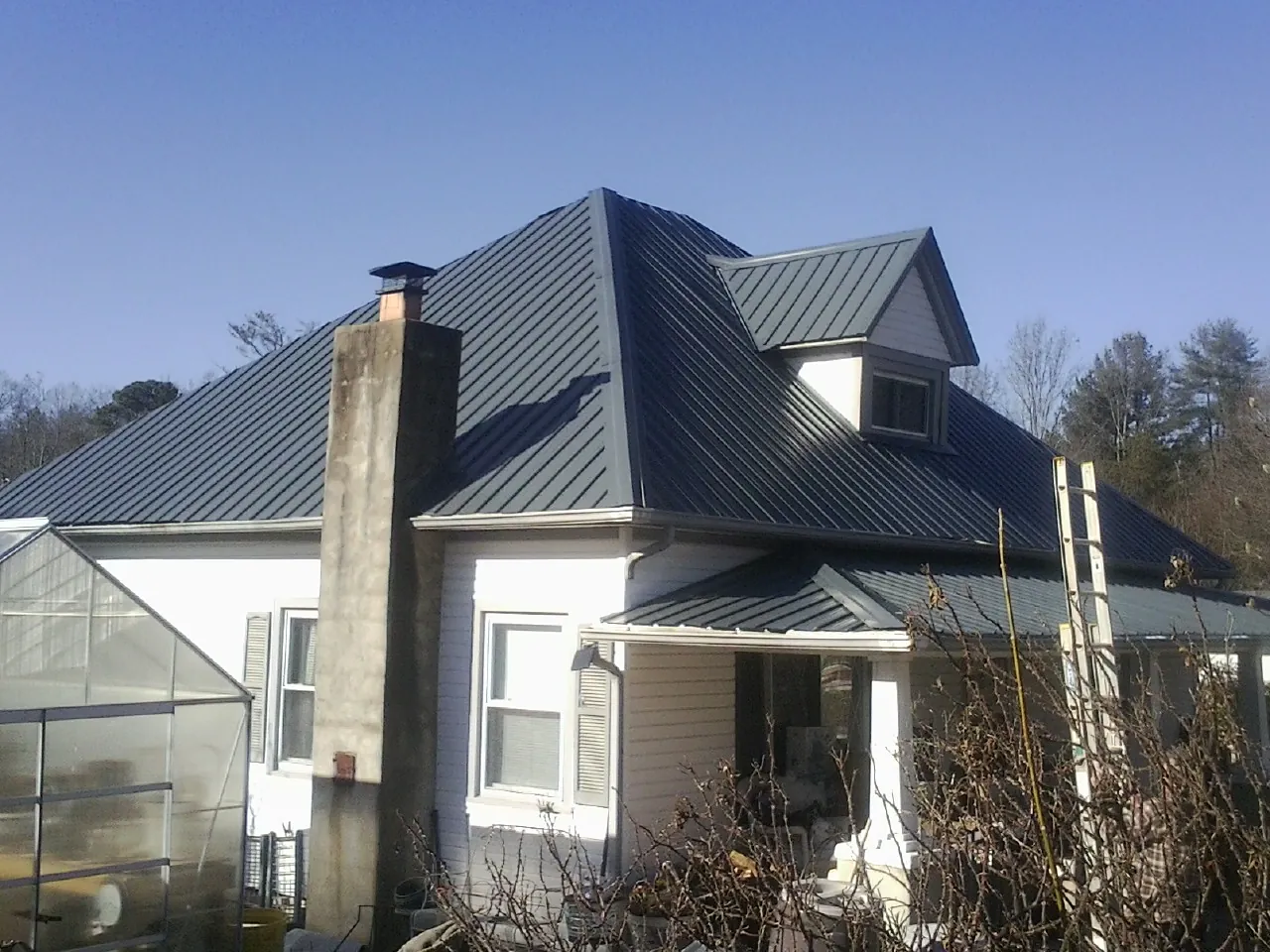 Dark blue standing seam metal roof on a white farmhouse with dormer — Slate & Tile Roof Repair by Roofing Brothers in Lamy