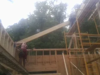 Carpenter raising a rafter beam on a new second story frame in Lamy