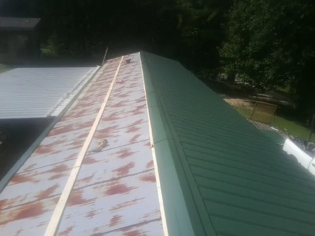 Old rusted panels beside newly installed green metal roofing — Wind Damage Roof Repair by Roofing Brothers in Lamy