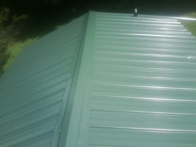 New green metal panels meeting at the ridge of a roof — Flat Roof Repair work by our crew in Lamy