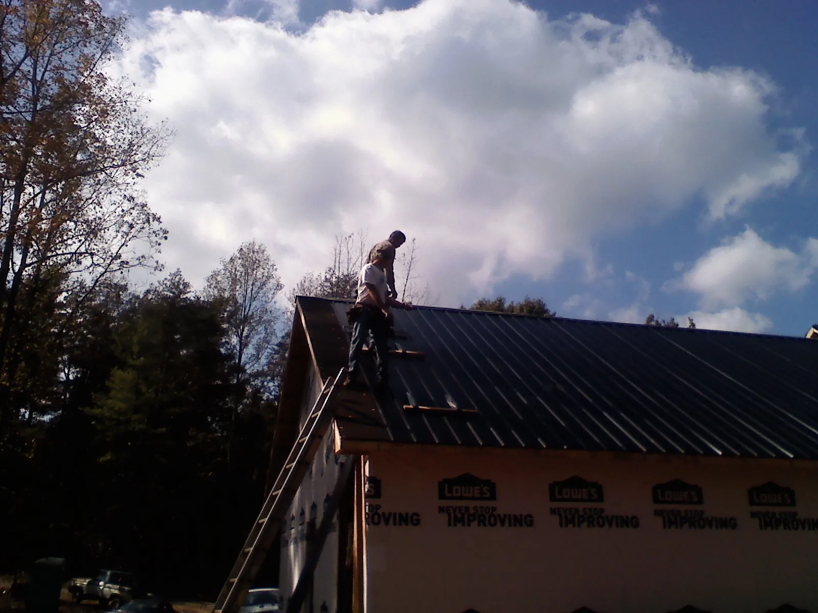 Roofer fastening dark metal panels high against a cloudy sky, from a Roof Inspection job in Lamy