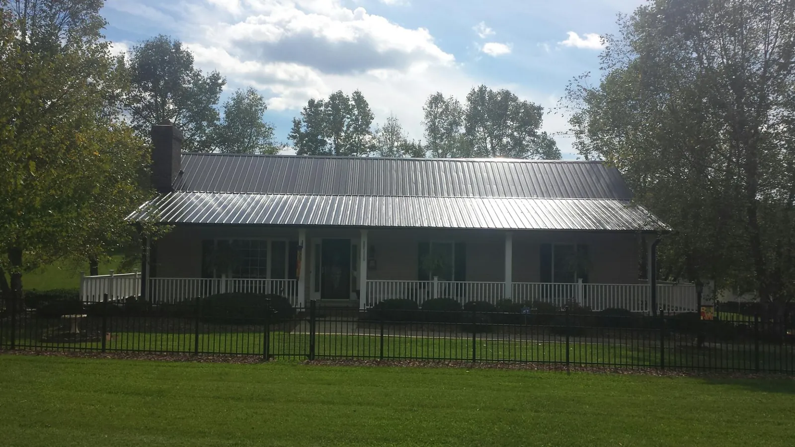 Gray metal roof on a brick ranch with a full width front porch — Gutter Guard Installation work by our crew in Lamy