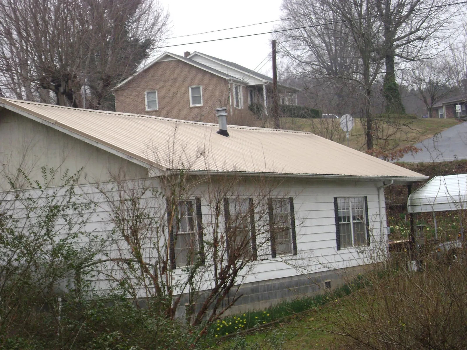 Tan metal roof on a white sided house set into a hillside — Commercial Roofing by Roofing Brothers in Lamy