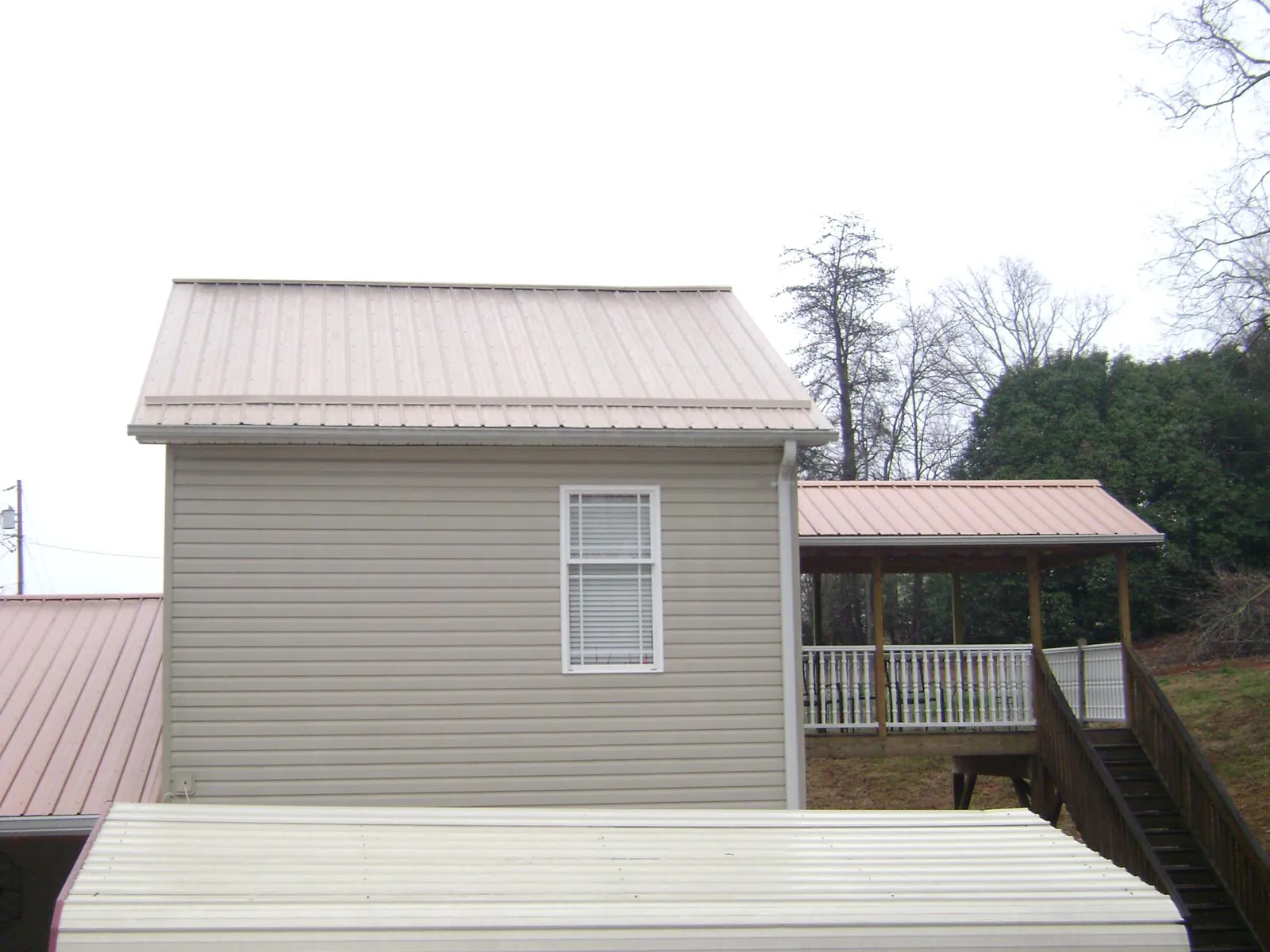 Tan metal roofs on a two story addition and attached porch, from a Roof Replacement job in Lamy
